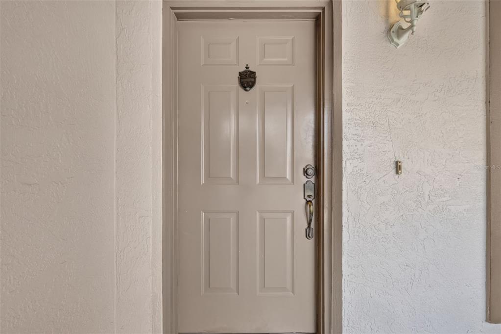 A beige front door with a door knocker and handle set is set in a wall — 1911 DEL NORTE DRIVE, THE VILLAGES, FL