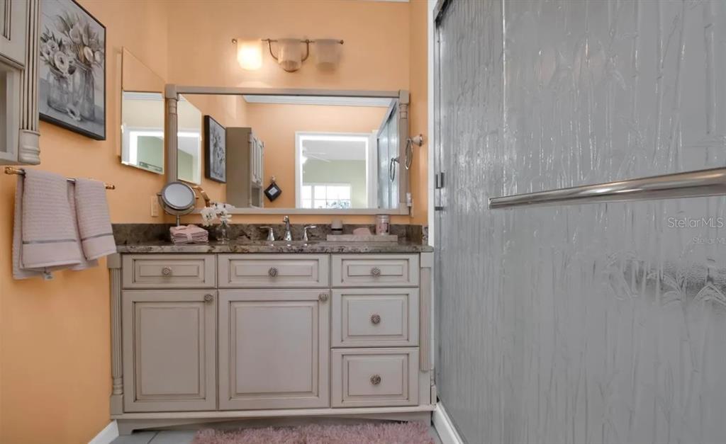 A bathroom features a light-colored vanity with a granite countertop, a mirror, and a shower — 19335 WATER OAK DRIVE UNIT 108, PORT CHARLOTTE, FL