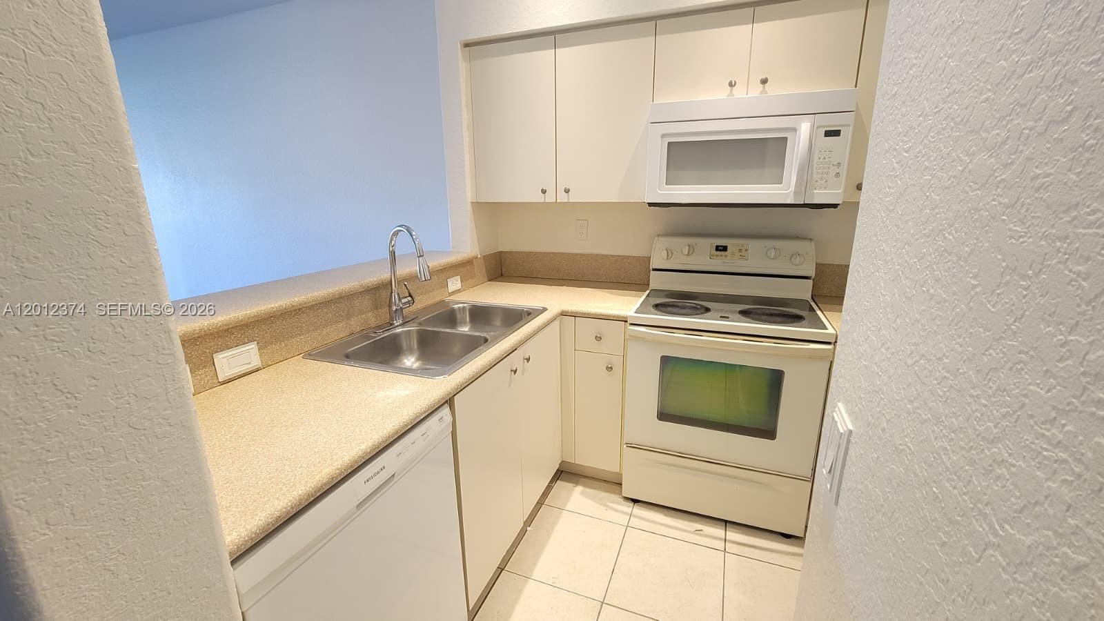 A small kitchen features white appliances, light-colored cabinets, and tan countertops — 8353 SW 26th St # 104, Miramar FL 33025, MIRAMAR, FL