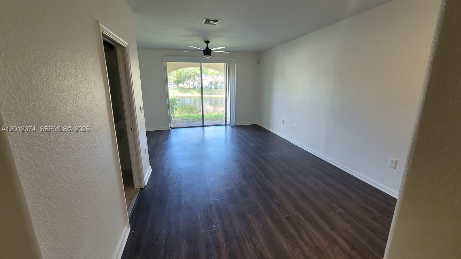 An empty living room features dark wood-look flooring, a ceiling fan, and sliding glass doors — 8353 SW 26th St # 104, Miramar FL 33025, MIRAMAR, FL