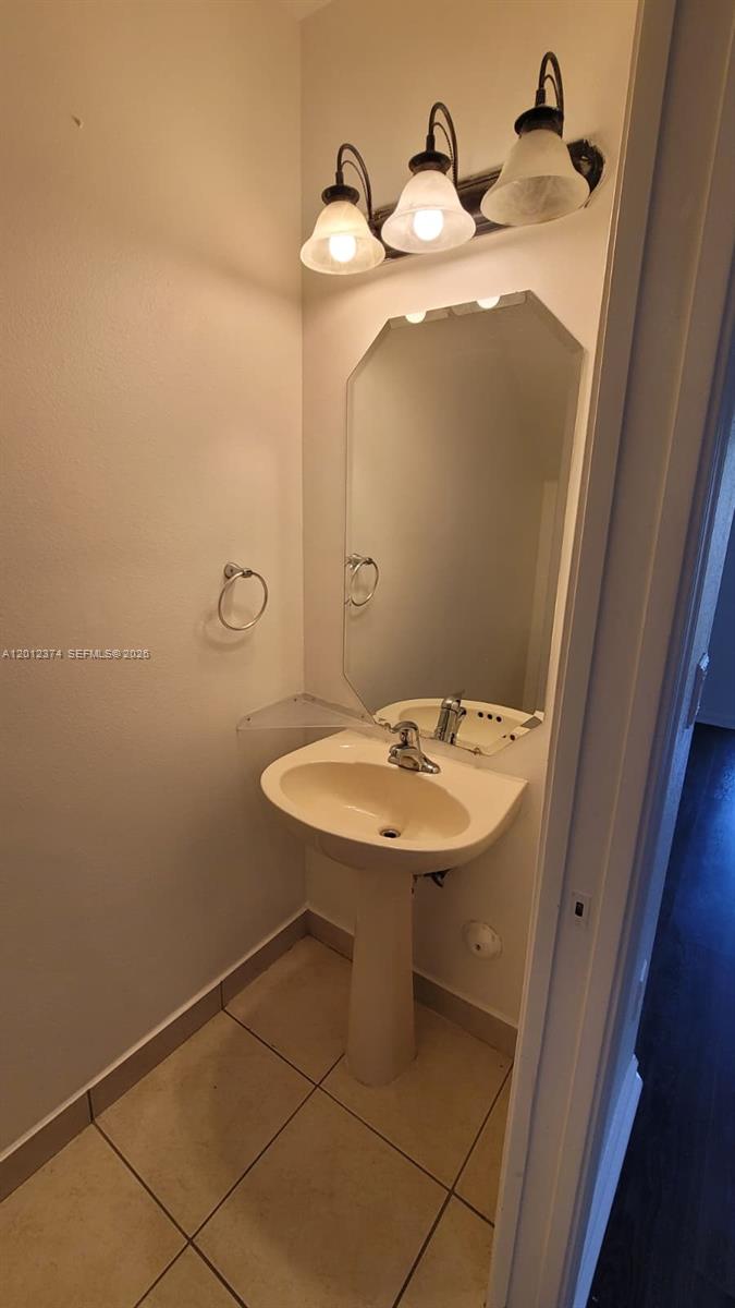 A small bathroom features a pedestal sink, a wall-mounted mirror, and a three-light fixture — 8353 SW 26th St # 104, Miramar FL 33025, MIRAMAR, FL