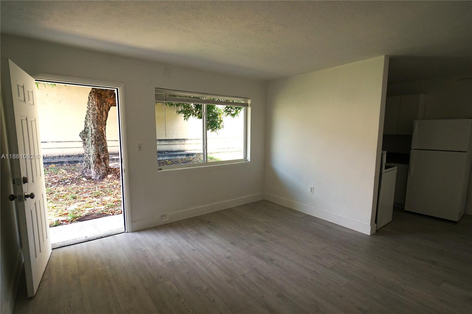 A room with light wood-look flooring, a white door, a window, and a kitchen area — 584 NW 65th St # 3, Miami FL 33150, MIAMI, FL
