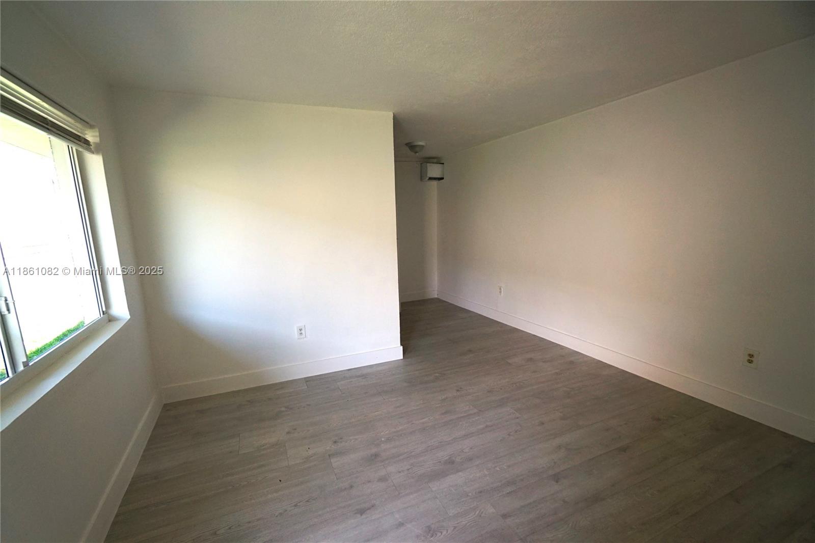 An empty room features white walls, light wood-look flooring, and a window on the left — 584 NW 65th St # 3, Miami FL 33150, MIAMI, FL