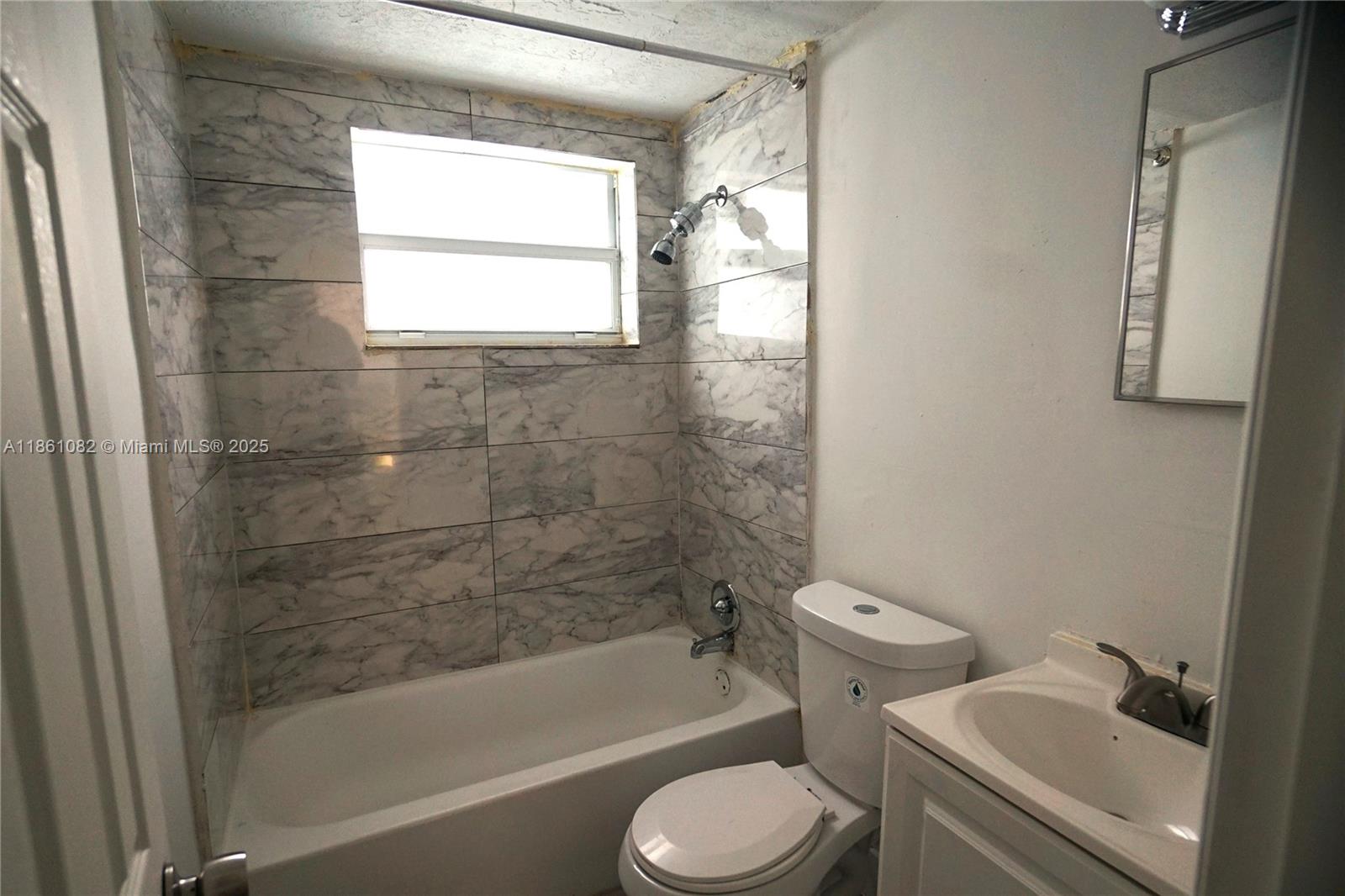 A bathroom features a white bathtub with marble-look tile walls, a toilet, and a vanity — 584 NW 65th St # 3, Miami FL 33150, MIAMI, FL