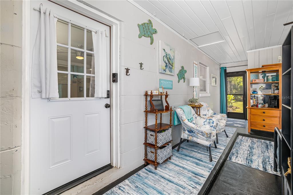 A sunroom features a white door, two patterned armchairs, a wooden shelf, and blue rugs — 1611 27TH STREET W, BRADENTON, FL