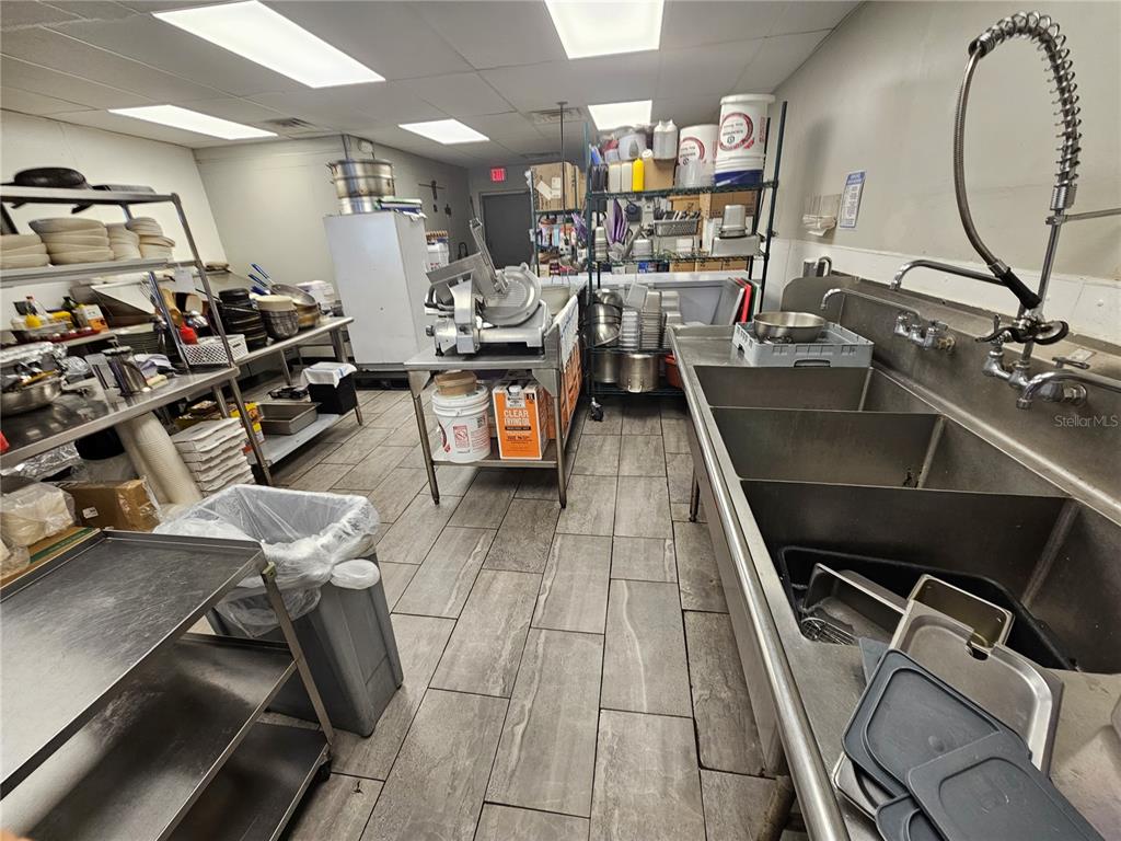 A commercial kitchen features stainless steel prep tables, a three-compartment sink, and tiled flooring — 6026 N US HWY41, APOLLO BEACH, FL
