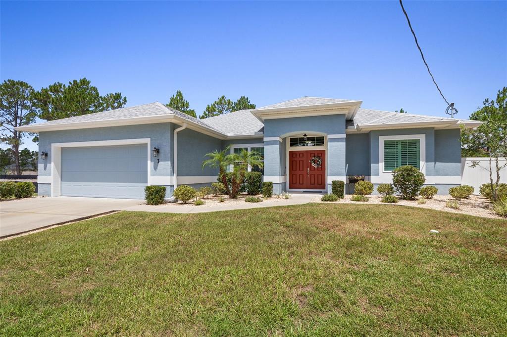 A single-story blue house with a two-car garage and a red front door — 3 LEEDS PLACE, PALM COAST, FL