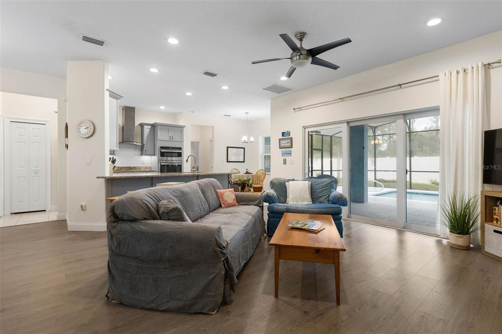 An open-concept living room features wood-look flooring, a gray sofa, and sliding doors to a pool — 3 LEEDS PLACE, PALM COAST, FL