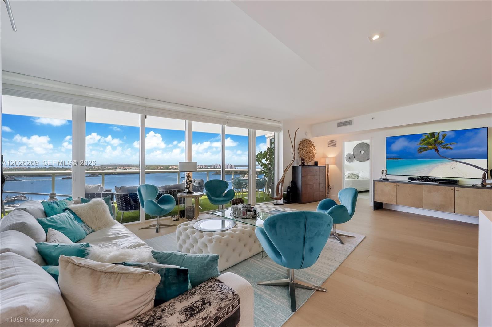 A modern living room features teal accent chairs, a white tufted ottoman, and floor-to-ceiling windows — 400 Alton Rd # 1506, Miami Beach FL 33139, MIAMI BEACH, FL