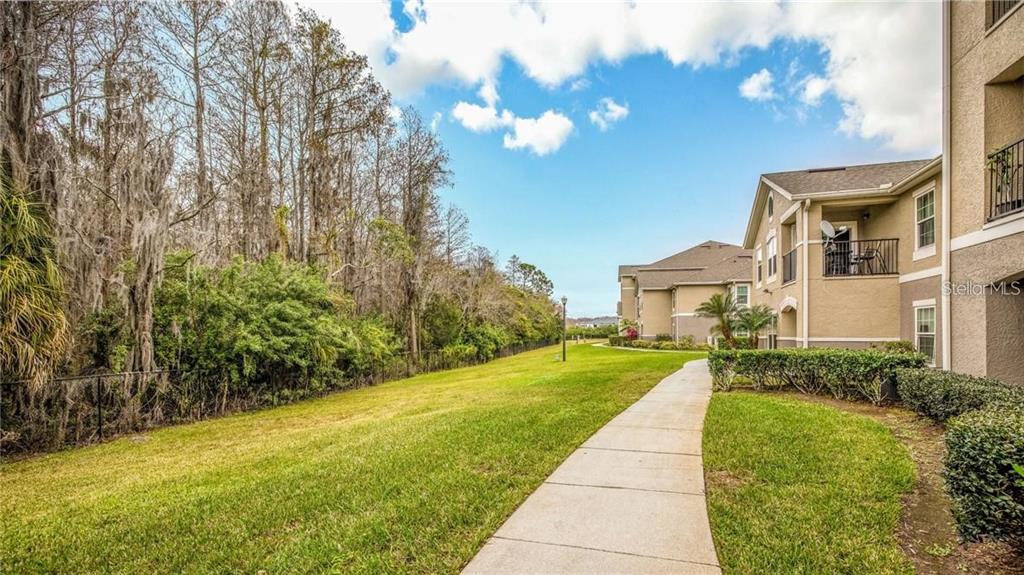 A concrete walkway runs alongside a multi-story apartment building next to a grassy lawn — 6530 SWISSCO DRIVE UNIT 1123, ORLANDO, FL