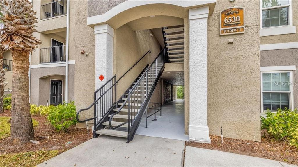 An exterior view of an apartment building entrance with a metal staircase and concrete walkway — 6530 SWISSCO DRIVE UNIT 1123, ORLANDO, FL