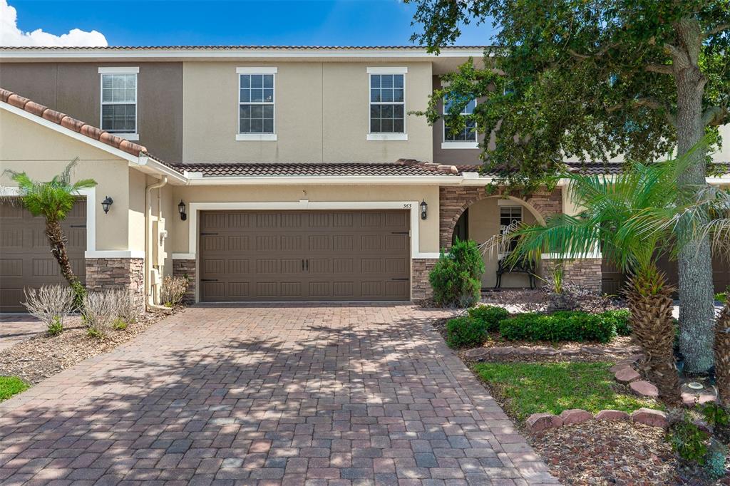 A two-story townhouse features a brown garage door, stone accents, and a brick paver driveway — 363 WHITE DOGWOOD LANE, OCOEE, FL