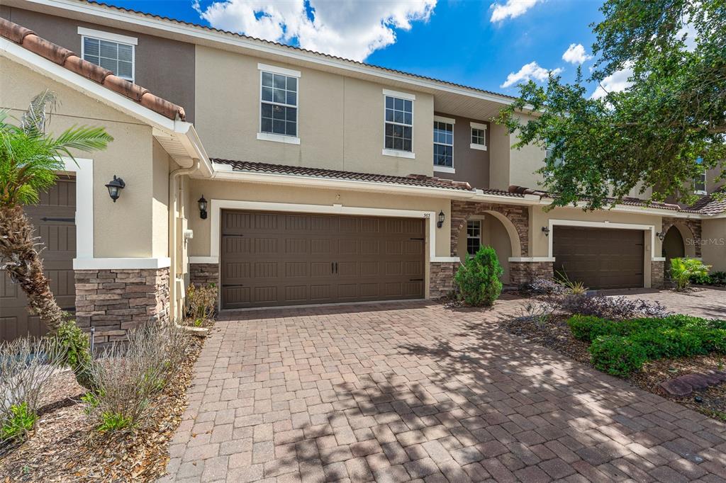 A two-story townhouse exterior features a paver driveway, brown garage doors, and stone accents — 363 WHITE DOGWOOD LANE, OCOEE, FL