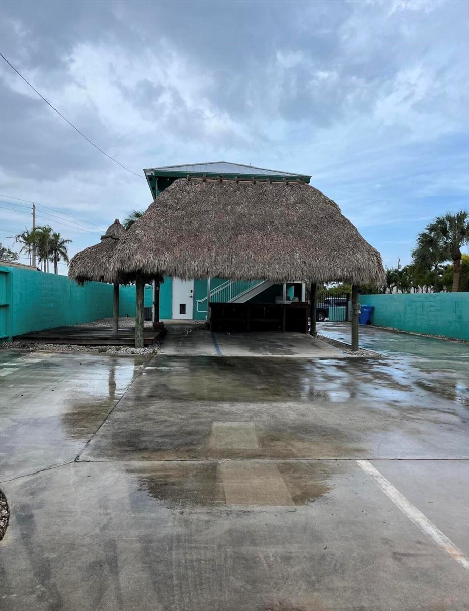 A large thatched-roof tiki bar structure sits on a concrete lot between teal walls — 112 Mayfield Road, Lantana FL 33462, LANTANA, FL