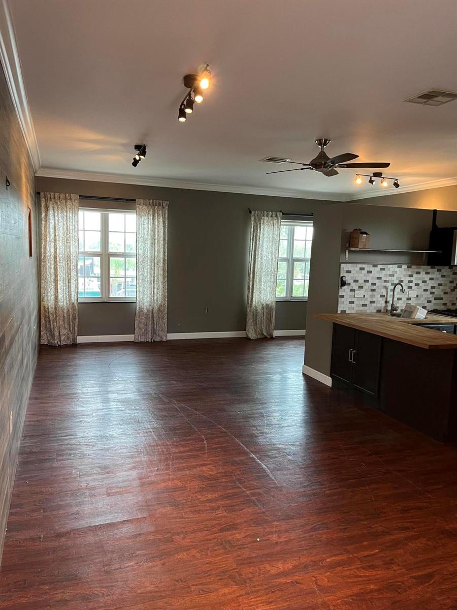 An open-concept living area features dark wood-look flooring, two windows with curtains, and a kitchen — 112 Mayfield Road, Lantana FL 33462, LANTANA, FL