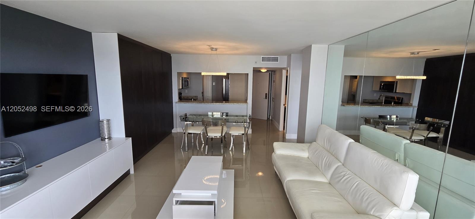 A living room features a white sofa, a glass dining table, and a wall-mounted television — 600 NE 36th St # 1509, Miami FL 33137, MIAMI, FL