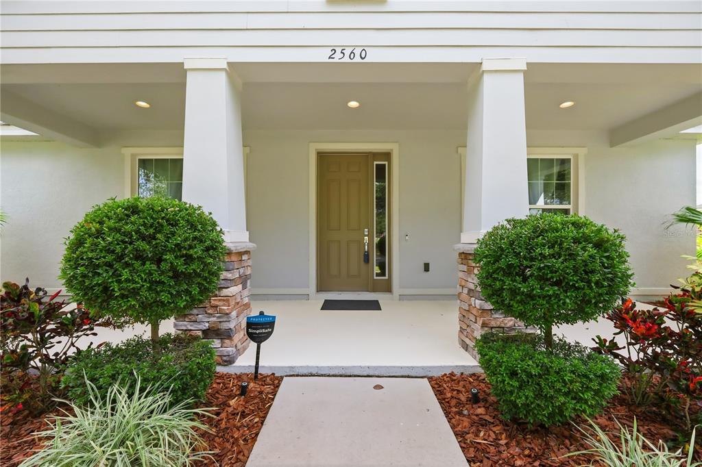 A front porch with two stone-based columns, a brown door, and two manicured round shrubs — 2560 GRASMERE VIEW PARKWAY S, KISSIMMEE, FL