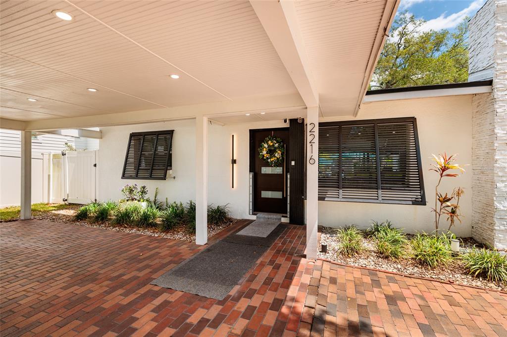 A brick driveway leads to a covered entryway with a dark front door and shutters — 2216 S OCCIDENT STREET, TAMPA, FL