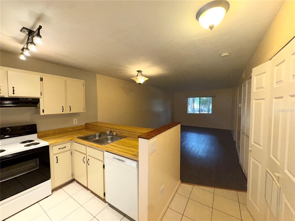 A kitchen with white cabinets and a wood-look countertop overlooks a living area — 109 SE 16TH AVENUE UNIT Q101, GAINESVILLE, FL