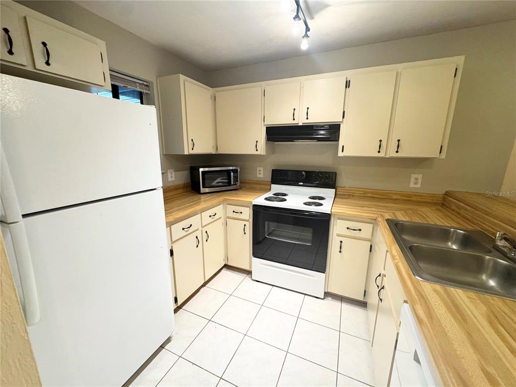 A kitchen features white appliances, light-colored cabinets, wood-look laminate countertops, and white tile flooring — 109 SE 16TH AVENUE UNIT Q101, GAINESVILLE, FL