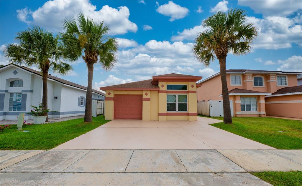 A single-story yellow house with a red garage door and two palm trees in front — 3222 BREWSTER DRIVE, KISSIMMEE, FL