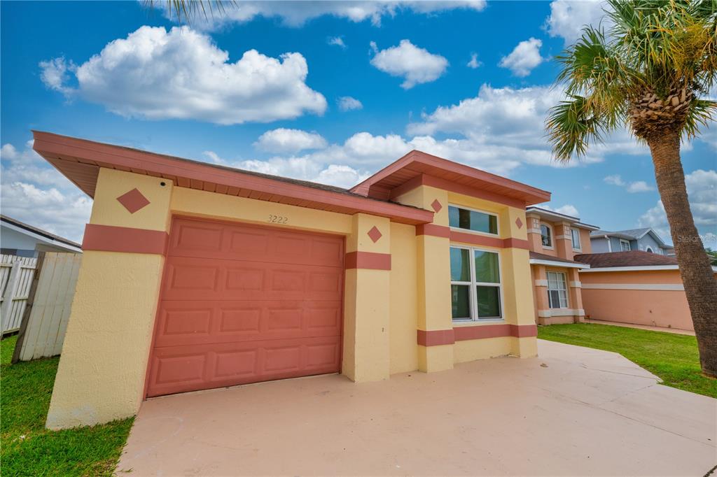 A yellow house with a red garage door and trim under a blue sky — 3222 BREWSTER DRIVE, KISSIMMEE, FL