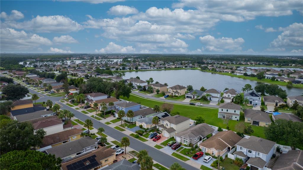 An aerial view shows a suburban neighborhood with houses, a large lake, and blue skies — 3222 BREWSTER DRIVE, KISSIMMEE, FL