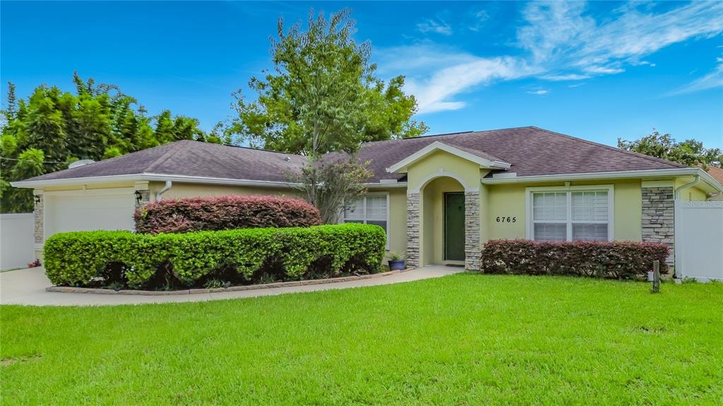 A single-story house with a light yellow exterior, stone accents, and a manicured front lawn — 6765 NW 14TH AVENUE, OCALA, FL