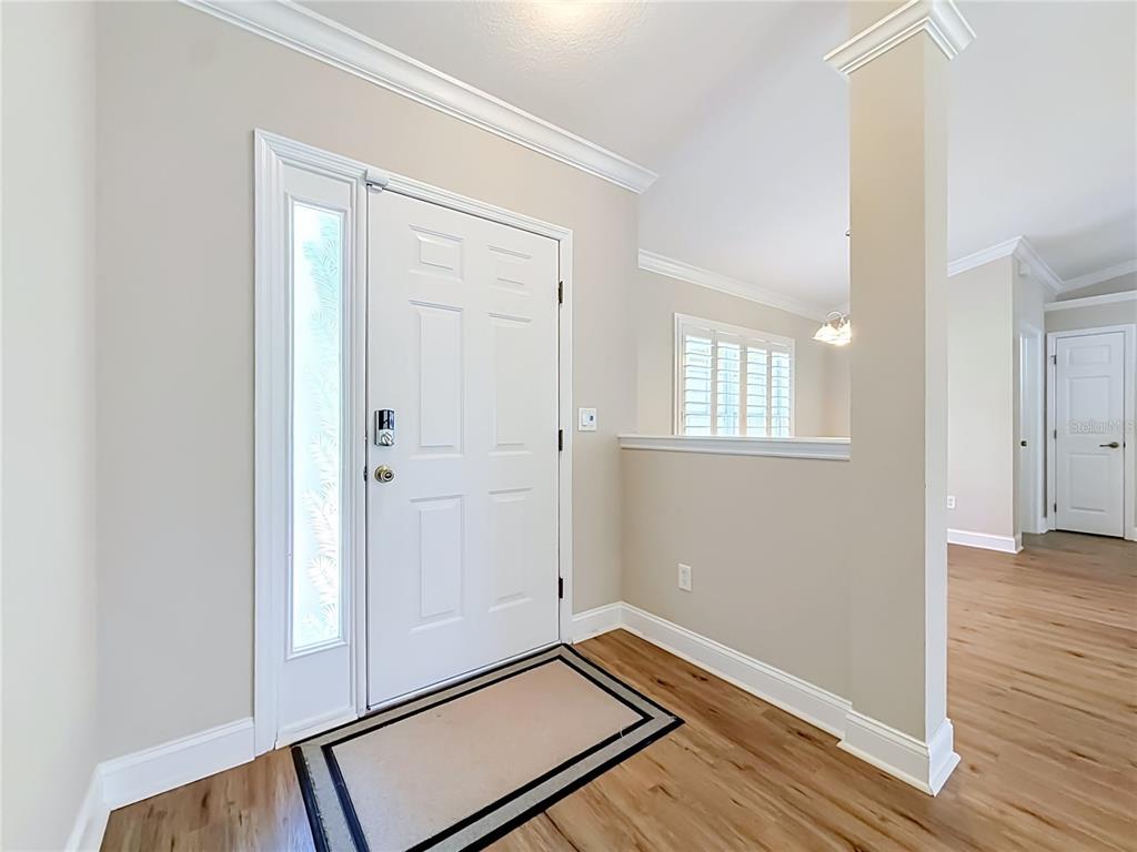 An entryway with a white front door, light wood flooring, and a partial wall — 6765 NW 14TH AVENUE, OCALA, FL