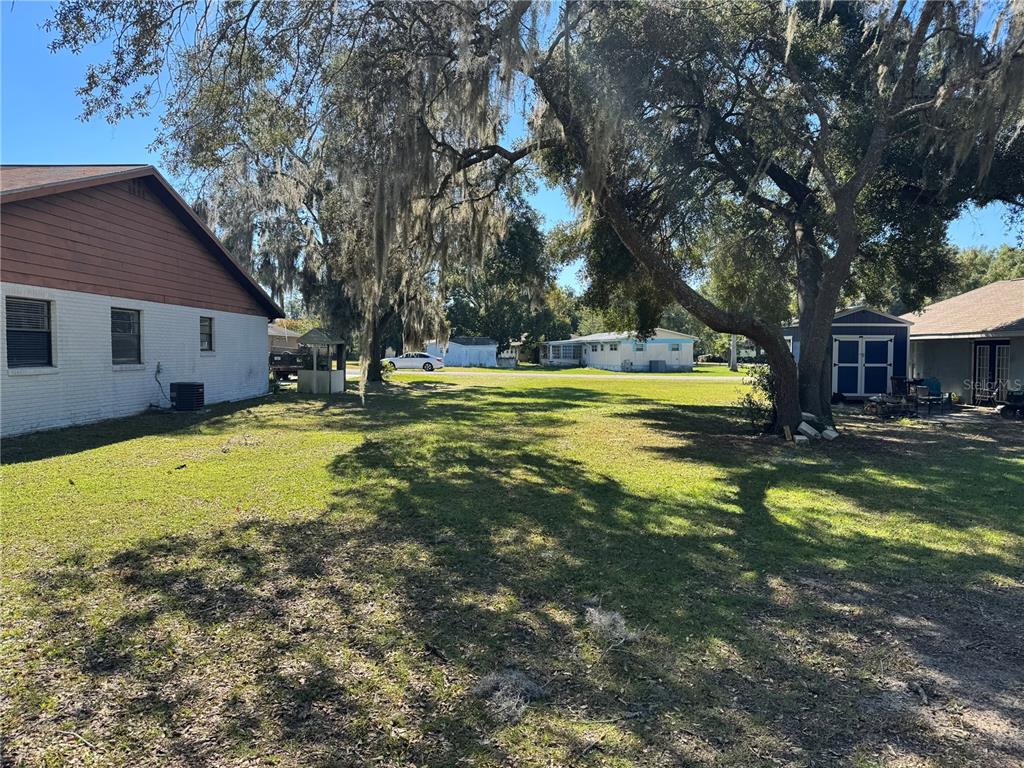 A grassy backyard features large oak trees, a white house, and a small blue shed — TBD SW 97TH STREET, OCALA, FL