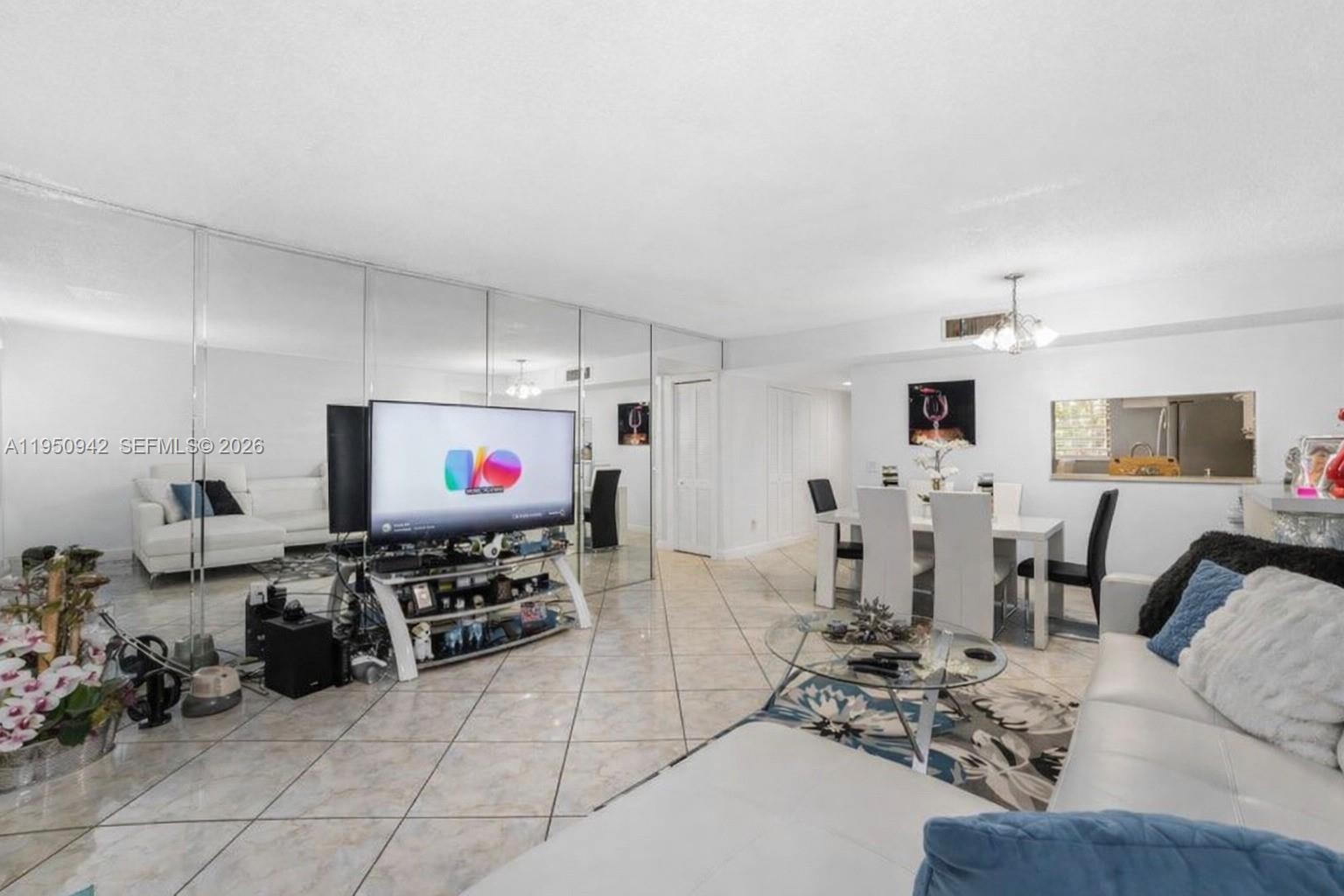 A living and dining area features mirrored walls, tile flooring, and white furniture — 8415 SW 107th Ave # 323W, Miami FL 33173, MIAMI, FL