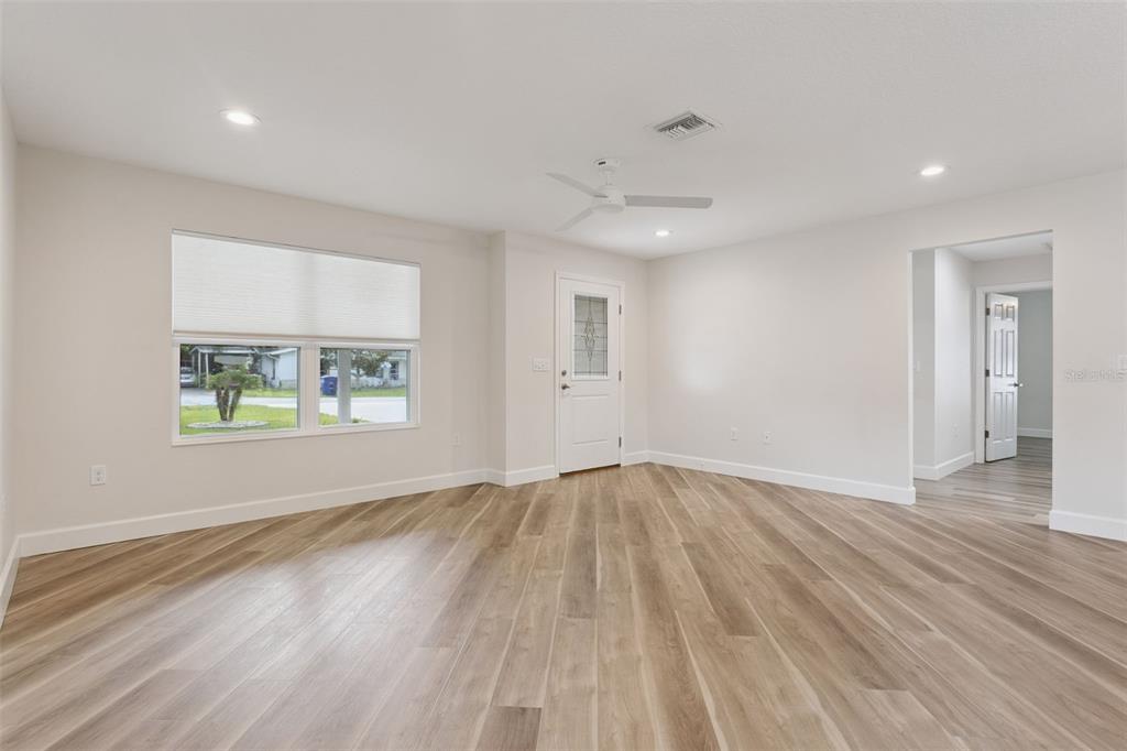 A bright, empty room features light wood-look flooring, a ceiling fan, and a front door — 209 JEAN STREET, TAVARES, FL