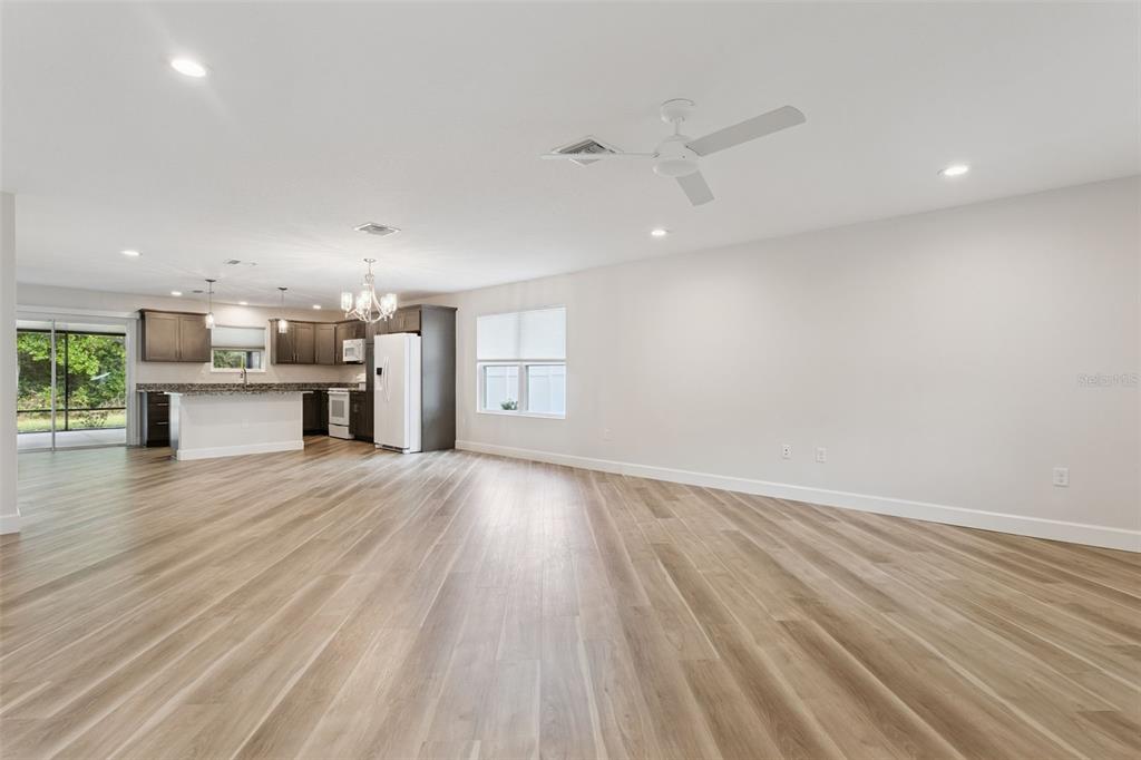 An open-concept kitchen and living area with light wood-look flooring and white walls — 209 JEAN STREET, TAVARES, FL