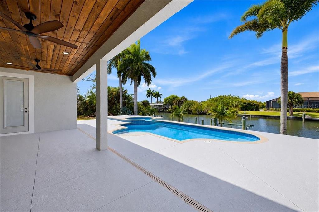 A covered patio overlooks a swimming pool and a canal lined with palm trees — 15408 MELPORT CIR, PORT CHARLOTTE, FL