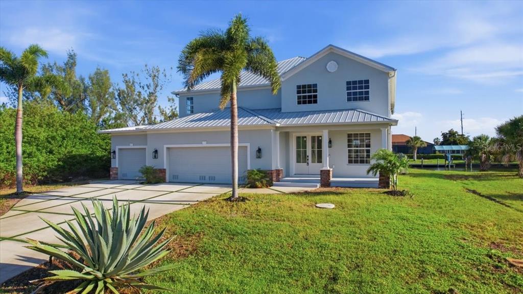 A two-story light blue house with a metal roof, three-car garage, and a palm tree — 15408 MELPORT CIR, PORT CHARLOTTE, FL
