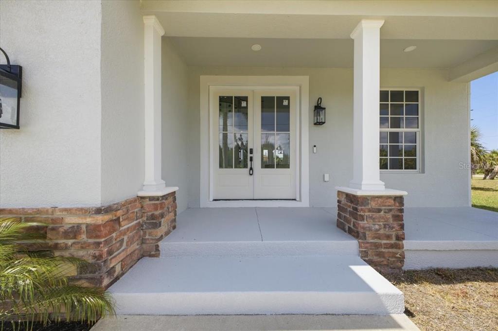 A covered front porch with stone-accented columns leads to a white double-door entryway — 15408 MELPORT CIR, PORT CHARLOTTE, FL