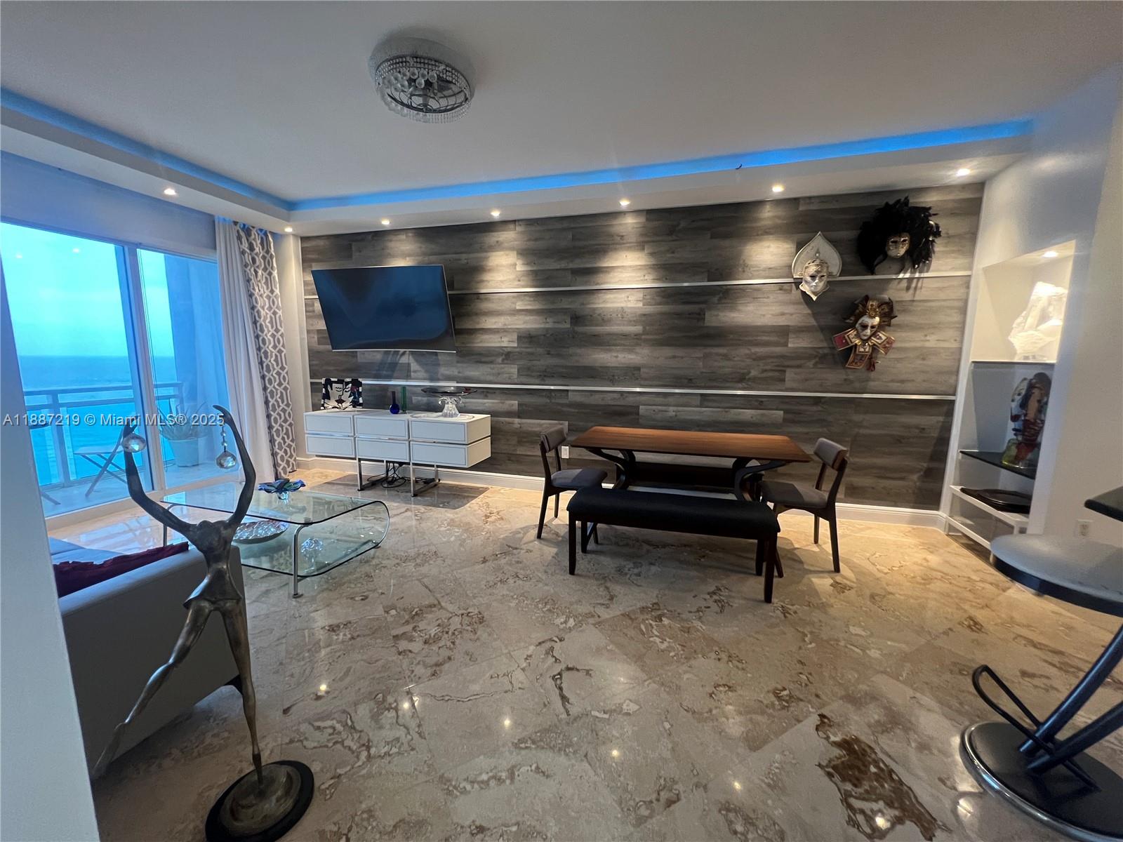 A living and dining area features wood-paneled walls, marble floors, and a balcony with ocean views — 6917 Collins Ave, Miami Beach FL 33141, MIAMI BEACH, FL