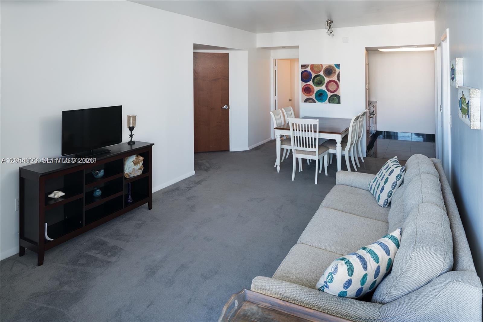 A living room with gray carpet features a dark wood media console and dining area — 6365 Collins Ave # 1811, Miami Beach FL 33141, MIAMI BEACH, FL