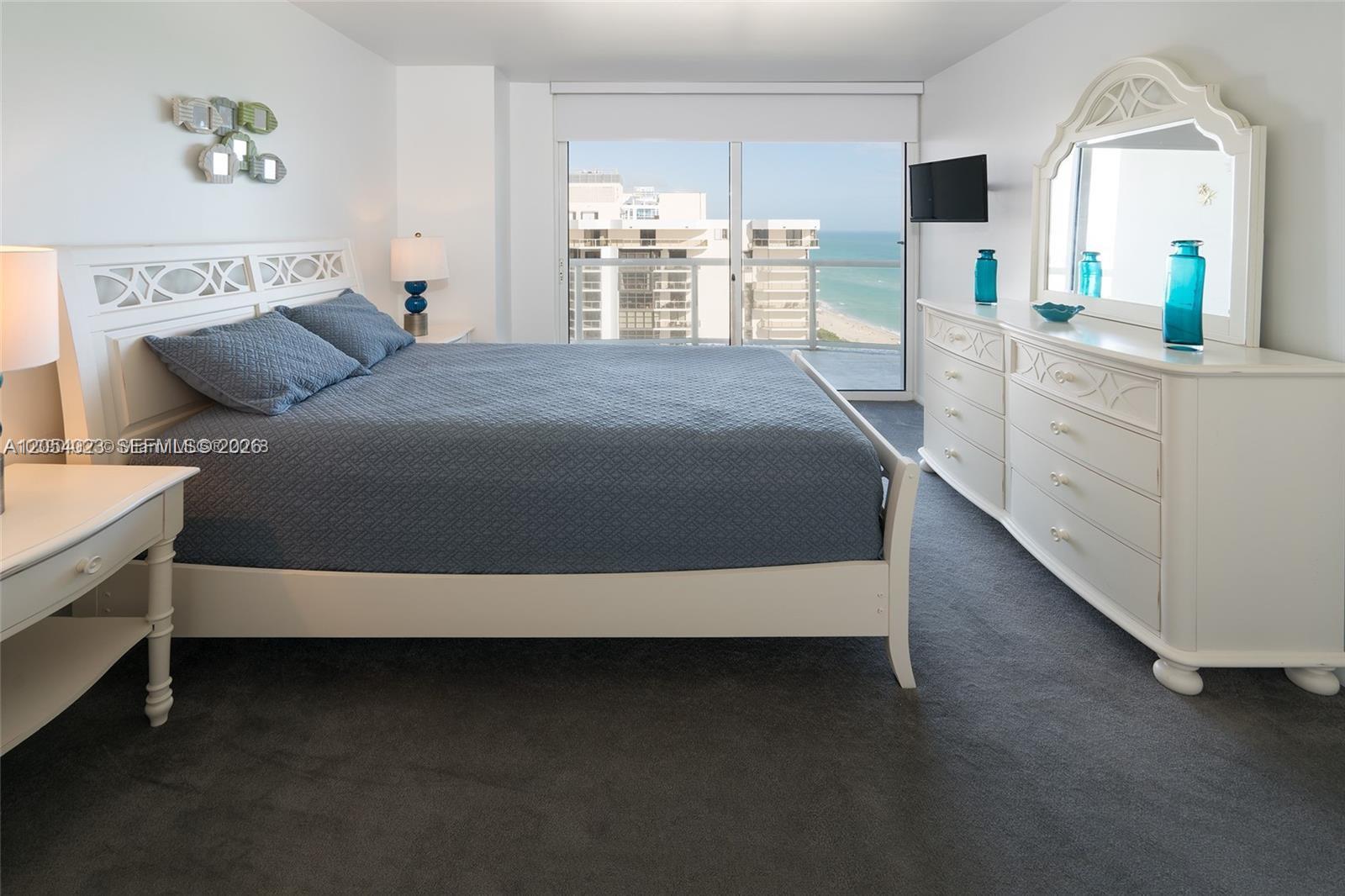 A bedroom features a white bed frame, matching dresser with mirror, and oceanfront balcony views — 6365 Collins Ave # 1811, Miami Beach FL 33141, MIAMI BEACH, FL