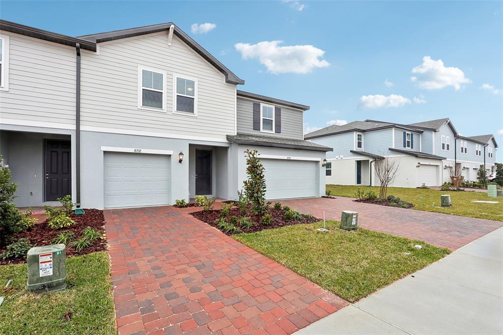 A two-story townhouse with a brick driveway, a garage, and light-colored siding — 16332 HAPPY EAGLE DRIVE, CLERMONT, FL