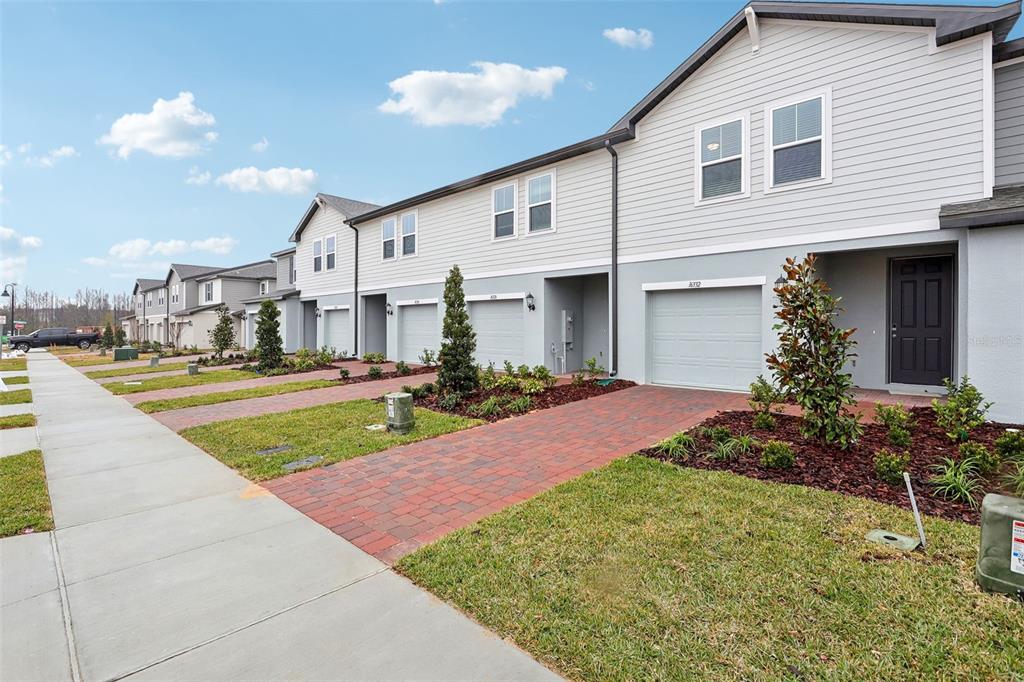 A row of modern townhouses with gray siding, brick driveways, and attached garages — 16332 HAPPY EAGLE DRIVE, CLERMONT, FL