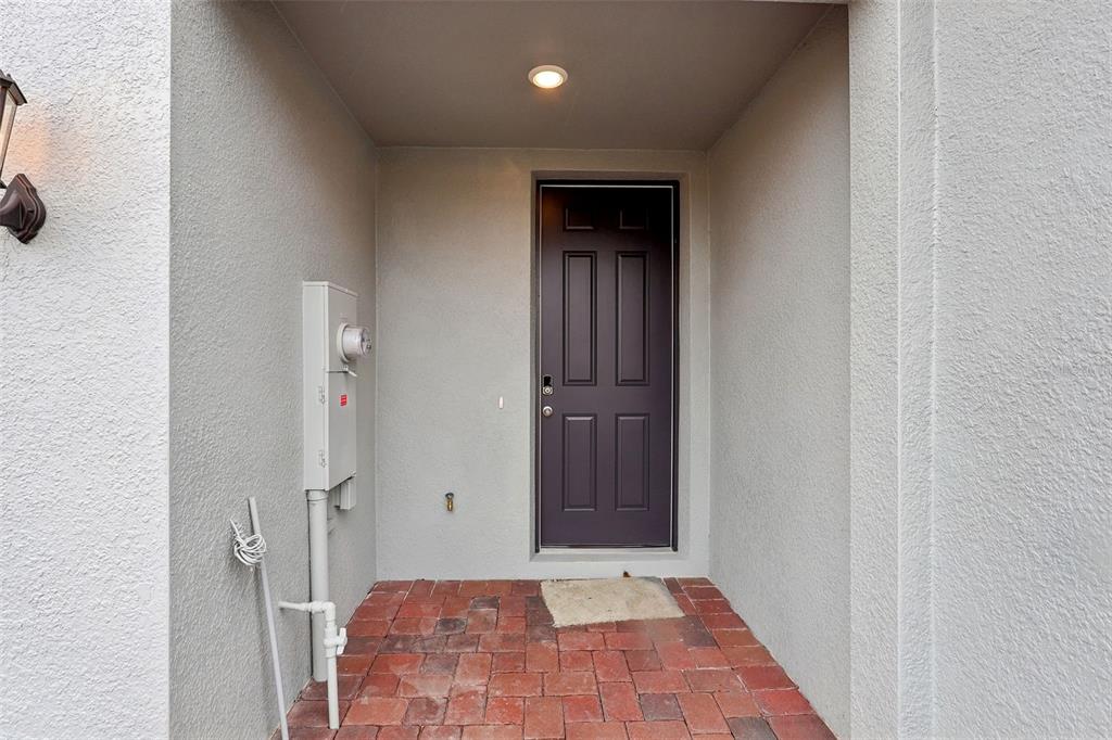 An exterior entryway features a dark brown door, a brick floor, and a utility box — 16332 HAPPY EAGLE DRIVE, CLERMONT, FL