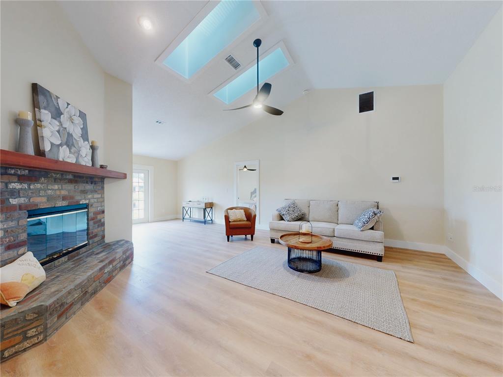 A living room features a brick fireplace, vaulted ceiling with skylights, and light wood flooring — 804 SOFT PINE COURT, NEW SMYRNA BEACH, FL