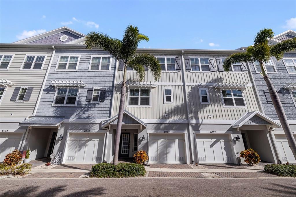 A row of multi-story townhomes with light-colored siding, attached garages, and palm trees in front — 6064 MOORINGS DRIVE S, ST PETERSBURG, FL