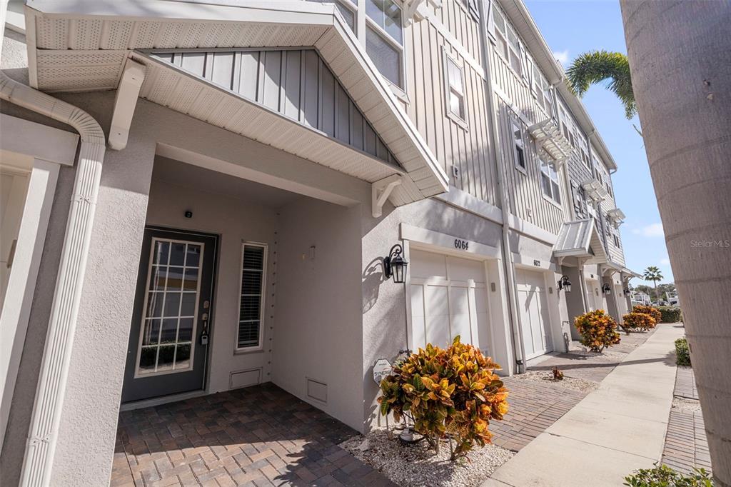 An exterior view of a multi-story townhouse with a brick walkway and garage — 6064 MOORINGS DRIVE S, ST PETERSBURG, FL
