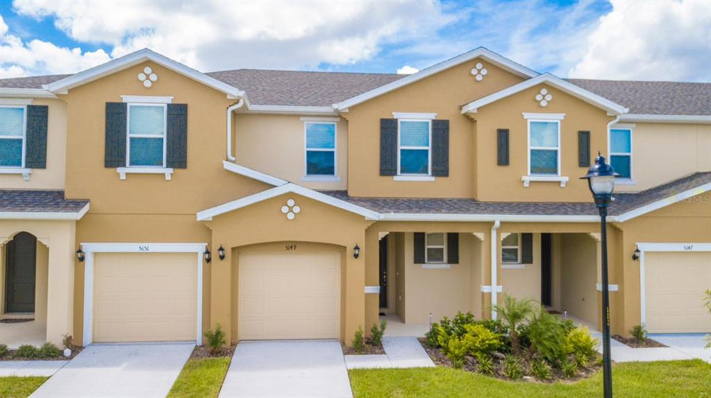 An exterior view of a multi-unit townhouse complex with tan stucco walls and beige garages — 5149 ADELAIDE DRIVE, KISSIMMEE, FL