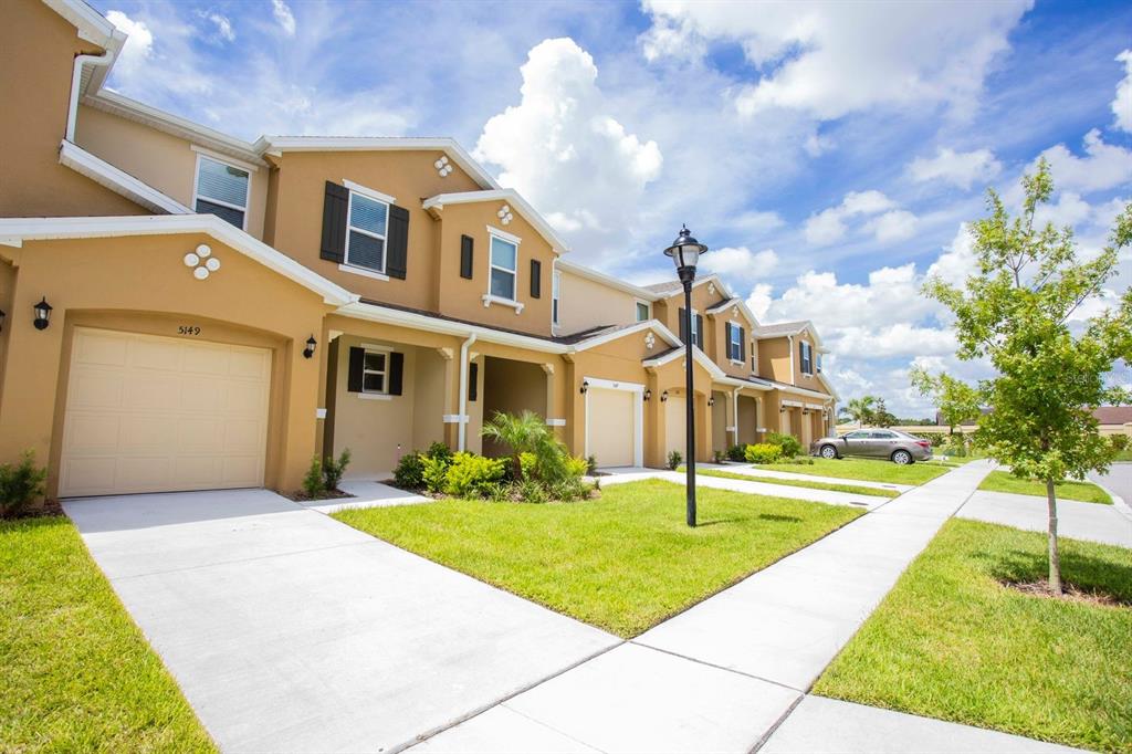 A row of tan townhouses with attached garages and concrete driveways under a blue sky — 5149 ADELAIDE DRIVE, KISSIMMEE, FL