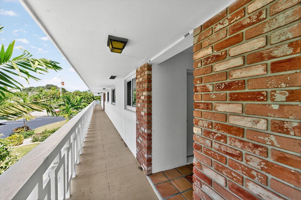 An outdoor apartment walkway features a brick-accented wall, a white railing, and a tiled floor — 331 Tequesta Drive # 224, Tequesta FL 33469, TEQUESTA, FL
