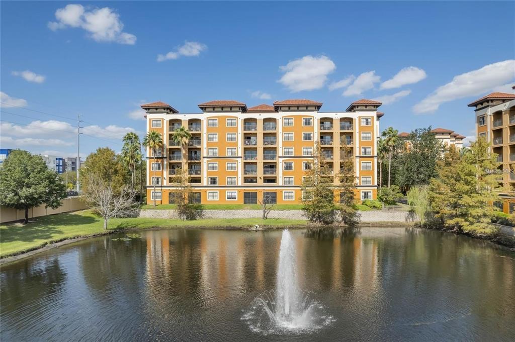 A multi-story apartment building with a fountain in the foreground pond under a blue sky — 12544 FLORIDAYS RESORT DR UNIT 202B, ORLANDO, FL