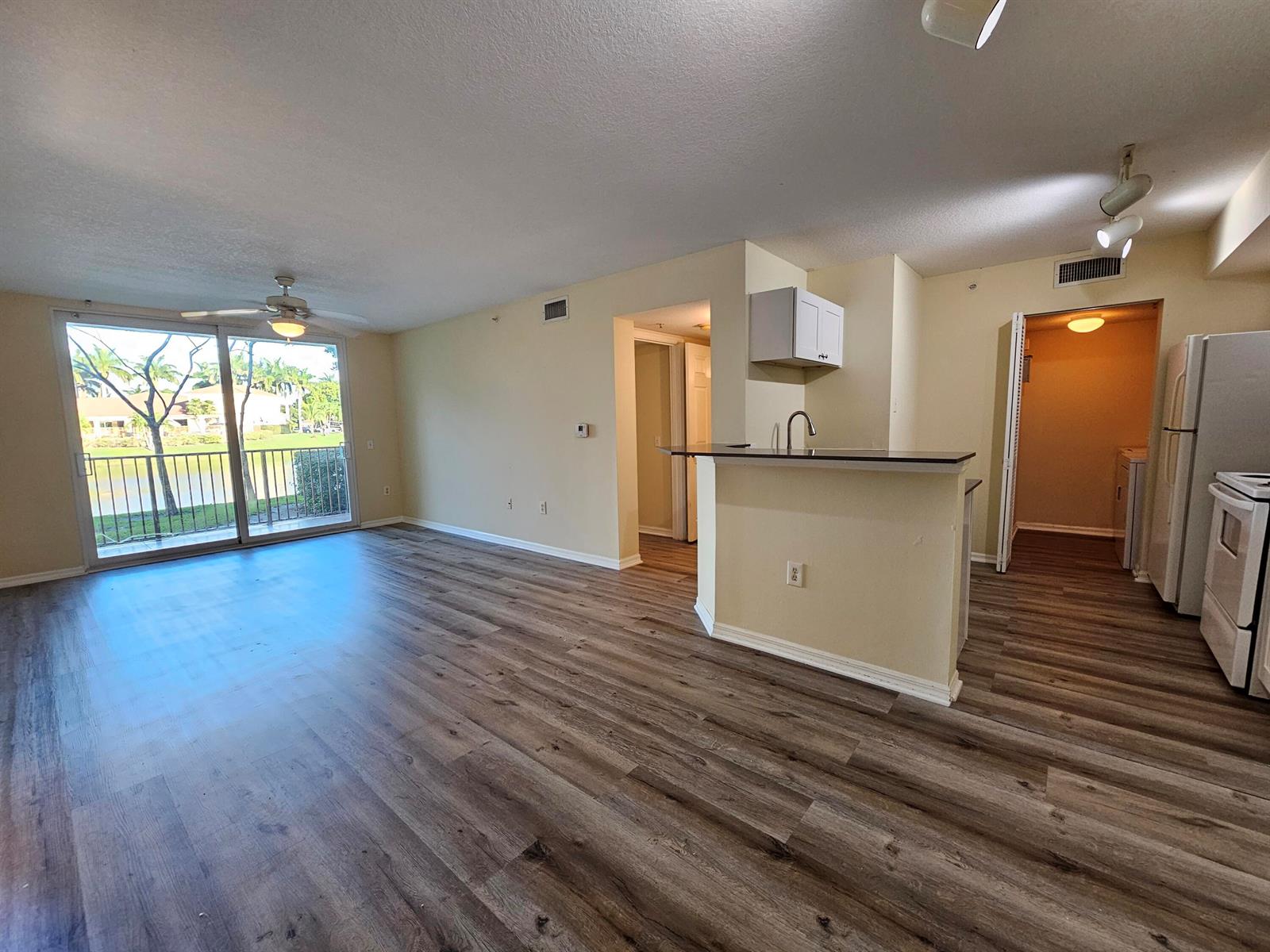 An open-concept living area features wood-look flooring, a kitchen island, and a sliding glass door — 604 Villa Circle # 604, Boynton Beach FL 33435, BOYNTON BEACH, FL